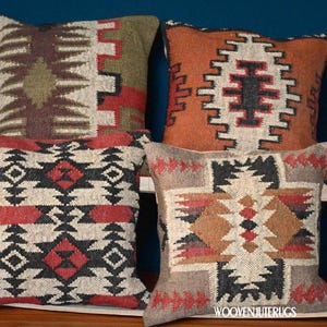 May include: Four decorative throw pillows with geometric patterns in shades of brown, red, black, and cream. The pillows are arranged on a wooden surface against a dark blue background. The pillows have a woven texture.
