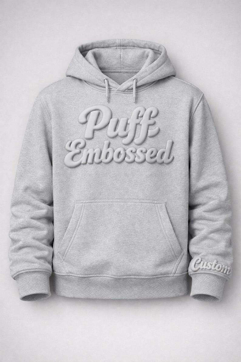 Puede incluir: Sudadera con capucha gris claro con las palabras "Puff Embossed" en relieve en el pecho. La sudadera tiene un bolsillo delantero y una capucha con cord&oacute;n. La palabra "Custom" est&aacute; bordada en el pu&ntilde;o.