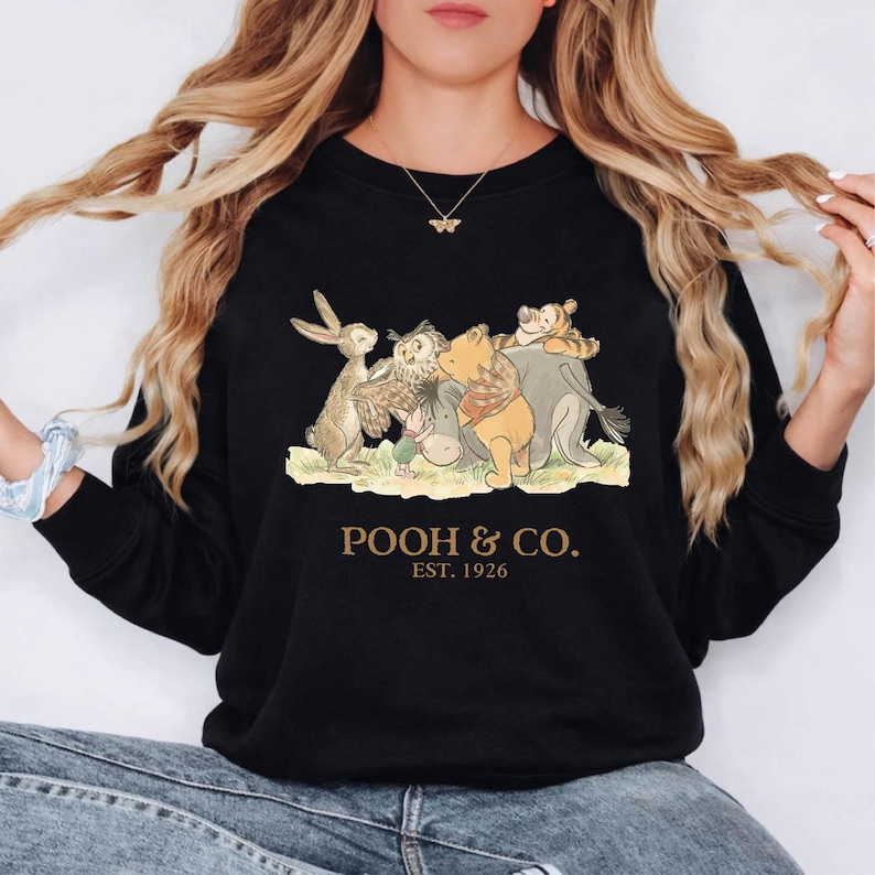 Puede incluir: Sudadera negra de cuello redondo con un dise&ntilde;o de Winnie the Pooh y sus amigos. El dise&ntilde;o incluye un conejo, un b&uacute;ho, un burro, Pooh y Tigger. El texto "POOH & CO. EST. 1926" est&aacute; impreso en dorado debajo.
