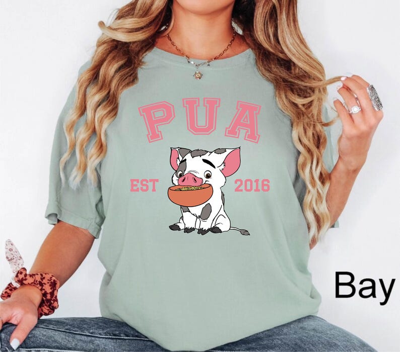 May include: A light green t-shirt featuring the word "PUA" in pink block letters above a cartoon pig holding a bowl of food. The text "EST 2016" is below the pig.