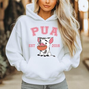 May include: White hooded sweatshirt with a front pocket. The sweatshirt features the word "PUA" in pink block letters above a cartoon pig holding a bowl. The text "EST 2016" is printed below the pig.