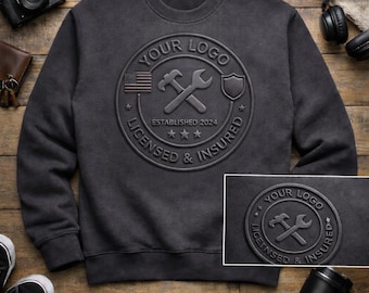Puede incluir: Sudadera gris oscuro con un logotipo en relieve 3D. El logotipo incluye un martillo, una llave inglesa, un escudo y la bandera estadounidense. El texto dice "YOUR LOGO", "LICENSED & INSURED" y "ESTABLISHED 2024". Las palabras "PREMIUM EMBOSSED LOGO" y "3D RAISED DESIGN" están en la parte inferior.