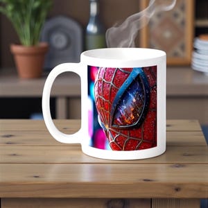 May include: White ceramic mug featuring a close-up of Spider-Man's mask, with red webbing and a blue eye. Steam rises from the mug, suggesting a hot beverage. The mug sits on a wooden table.