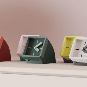 Może przedstawiać: Kolekcja pięciu klinowych zegarów analogowych w różnych kolorach, w tym terakoty, jasnego różu, ciemnej zieleni, żółci i bieli. Każdy zegar posiada kwadratową tarczę z prostymi oznaczeniami godzin i dwiema wskazówkami ustawionymi pod kątem.