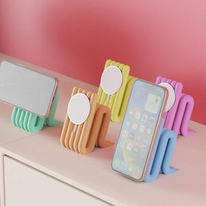 Könnte beinhalten: Eine Sammlung von vier Handyhaltern aus Silikon in den Farben Minzgrün, Pfirsich, Limettengrün und Lavendel. Jeder Halter hat ein flexibles, geripptes, schlangenförmiges Design mit einem runden magnetischen Ladepad an der Vorderseite.