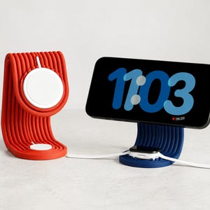 Könnte beinhalten: Ein roter und ein blauer gerippter Ladeständer für Mobilgeräte. Der rote Ständer verfügt über ein weißes, kreisförmiges magnetisches Ladegerät. Der blaue Ständer hält ein Smartphone mit der Uhrzeit 11:03 in großer blauer Schrift und eine weiße Smartwatch.