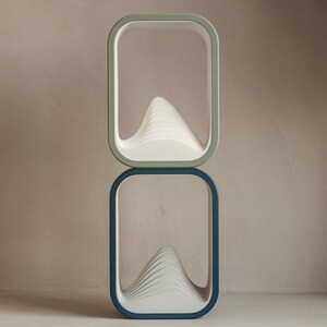 Puede incluir: Dos estantes rectangulares apilados con esquinas redondeadas. El estante superior tiene un marco verde claro y el estante inferior tiene un marco azul oscuro. Cada estante contiene una estructura blanca en forma de ola.