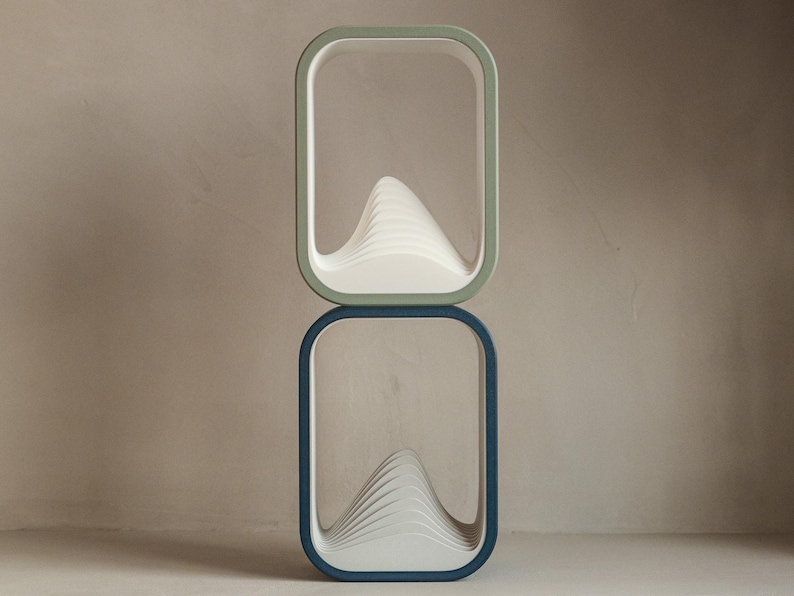 Puede incluir: Dos estantes rectangulares apilados con esquinas redondeadas. El estante superior tiene un marco verde claro y el estante inferior tiene un marco azul oscuro. Cada estante contiene una estructura blanca en forma de ola.
