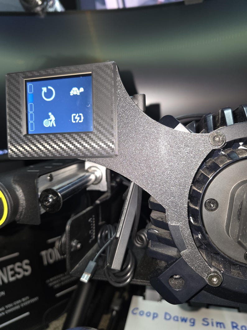 Pu&ograve; includere: Un supporto per display con texture in fibra di carbonio nera fissato a una base per volante da sim racing. Lo schermo rettangolare mostra quattro icone bianche: una freccia di aggiornamento, una tartaruga, una persona con ruota e un fulmine.