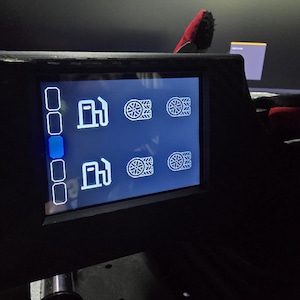 Pu&ograve; includere: Uno schermo digitale nero con un'interfaccia blu scuro e icone a linee bianche. Lo schermo mostra due file di simboli di pompe di benzina abbinati a icone di pneumatici e una colonna verticale di cinque riquadri di selezione a sinistra.