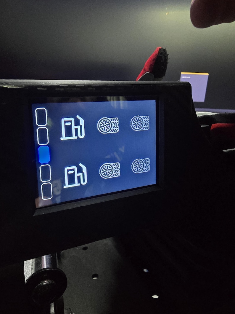 Pu&ograve; includere: Uno schermo digitale nero con un'interfaccia blu scuro e icone a linee bianche. Lo schermo mostra due file di simboli di pompe di benzina abbinati a icone di pneumatici e una colonna verticale di cinque riquadri di selezione a sinistra.