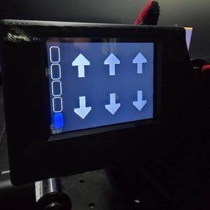 Pu&ograve; includere: Un pannello di controllo elettronico nero con uno schermo rettangolare dall'interfaccia blu. Il display mostra una colonna verticale di quattro riquadri bianchi, con quello in basso riempito di blu, e sei frecce bianche rivolte verso l'alto e il basso.