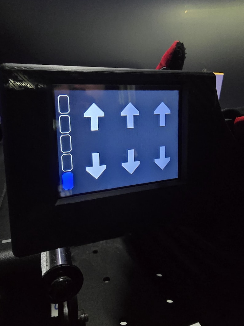 Pu&ograve; includere: Un pannello di controllo elettronico nero con uno schermo rettangolare dall'interfaccia blu. Il display mostra una colonna verticale di quattro riquadri bianchi, con quello in basso riempito di blu, e sei frecce bianche rivolte verso l'alto e il basso.