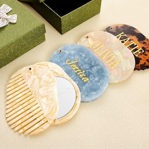 May include: Oval-shaped compact mirrors and a comb, some personalised with names in gold lettering. One mirror has a tortoiseshell pattern. A comb and a gift box are also present. Measurements are in centimetres.