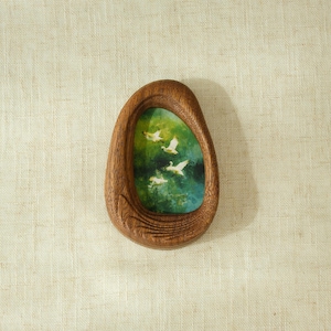 May include: A wooden framed art piece with an oval shape. The artwork inside depicts white birds in flight against a green and blue background. The frame is a warm brown color.