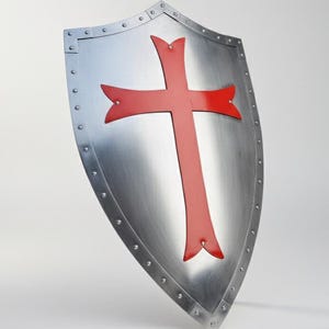 May include: A heater-style shield made of polished silver-toned metal featuring a prominent red cross emblem centered on the front. The shield is bordered by a metal rim secured with visible rivets along the entire outer edge of the surface.
