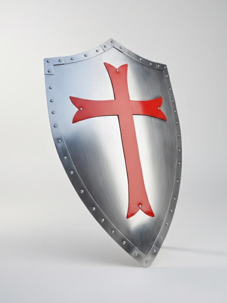 May include: A heater-style shield made of polished silver-toned metal featuring a prominent red cross emblem centered on the front. The shield is bordered by a metal rim secured with visible rivets along the entire outer edge of the surface.