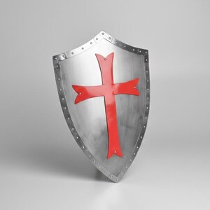 May include: A heater-style shield made of polished silver-toned metal featuring a prominent red cross centered on the front surface. The shield has a reinforced border secured with visible metal rivets along the entire outer edge of the structure.