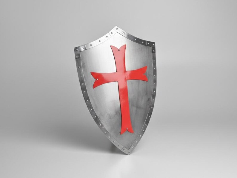 May include: A heater-style shield made of polished silver-toned metal featuring a prominent red cross centered on the front surface. The shield has a reinforced border secured with visible metal rivets along the entire outer edge of the structure.