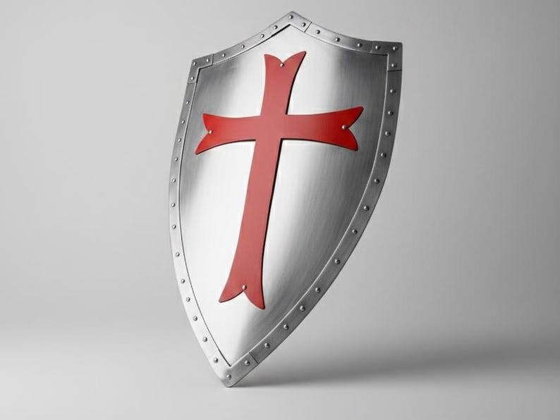 May include: A silver-colored heater shield featuring a prominent red cross emblem centered on its surface. The shield has a metallic finish with a reinforced border secured by a series of evenly spaced rivets along the entire outer edge.