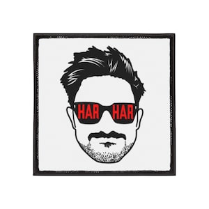 Może przedstawiać: Kwadratowa naszywka z czarną obwódką. Przedstawia czarno-białą ilustrację twarzy mężczyzny. Okulary przeciwsłoneczne mają czerwony napis "HAR HAR". Mężczyzna ma brodę i wąsy.