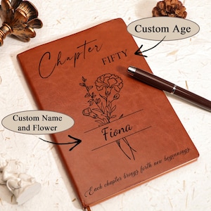 May include: A brown leather journal with the word "Chapter" and "FIFTY" engraved on the cover. The journal features a floral design and the name "Fiona". The text "Each chapter brings forth new beginnings" is also visible.