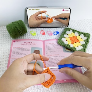 May include: Image of a crochet project in progress, featuring a smartphone showing a tutorial, green yarn, stitch markers, and a completed granny square. The image also shows a crochet hook and a pattern book.