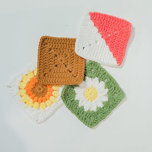 May include: Four colourful, square crochet pieces. One is brown, one has a sunflower design with yellow and orange petals, one has a white and coral diagonal design, and the last has a white daisy on a green background.