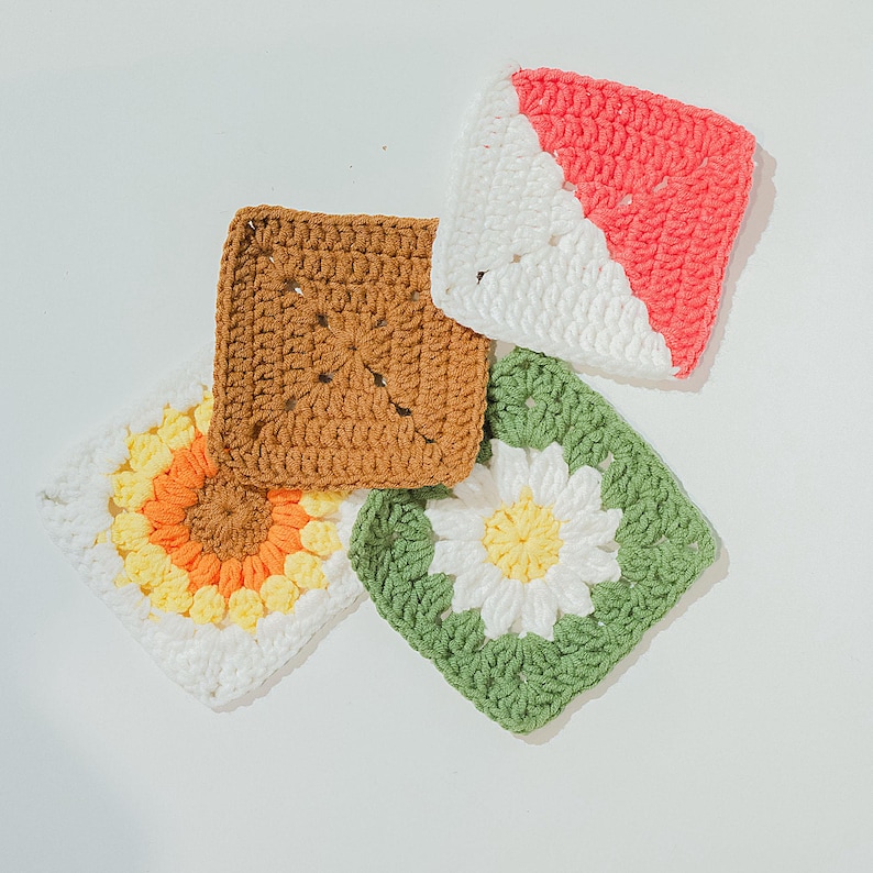 May include: Four colourful, square crochet pieces. One is brown, one has a sunflower design with yellow and orange petals, one has a white and coral diagonal design, and the last has a white daisy on a green background.
