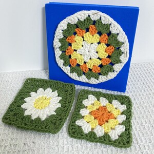 May include: A selection of handmade crochet items. The image shows a large, round, colourful doily and two square coasters. The doily is white, green, yellow, and orange. The coasters have a daisy and floral design.