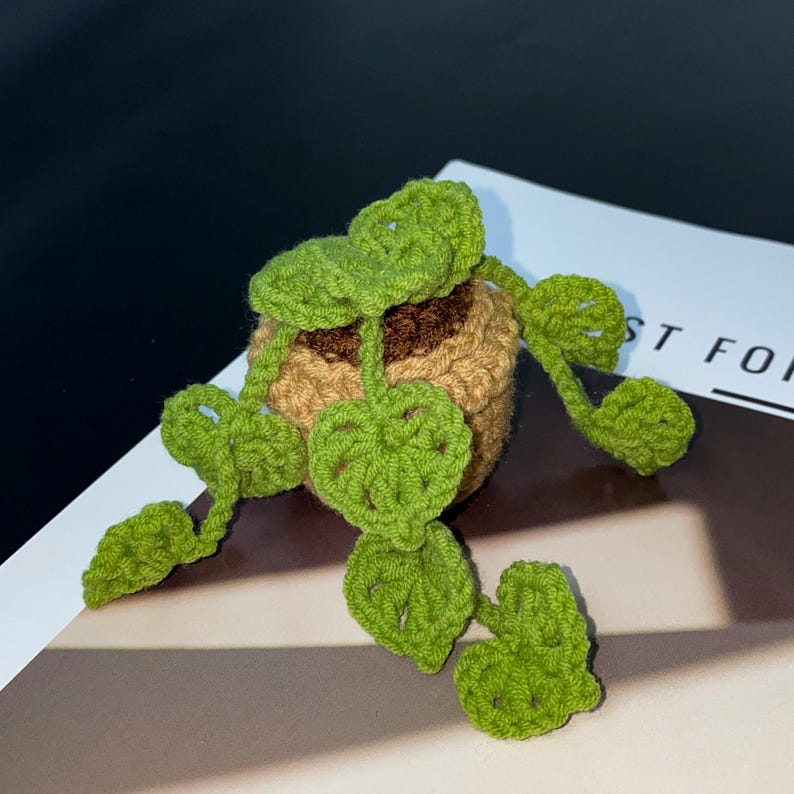 Puede incluir: Una planta de ganchillo en una maceta marr&oacute;n con hojas verdes. Las hojas tienen forma de coraz&oacute;n. La planta est&aacute; sobre una superficie blanca con el texto "ST FOR" visible.