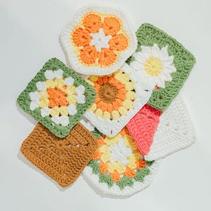 May include: A selection of colourful, handmade crochet squares in various floral and geometric designs. The squares feature a mix of colours, including white, orange, yellow, green, and brown. The crochet work is detailed and intricate, showcasing a variety of patterns.