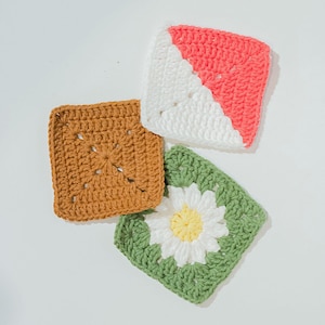 May include: Four handmade crochet squares in different colours. One is brown, another is white and coral, and the third is green with a white and yellow daisy. Ideal for crafting projects.