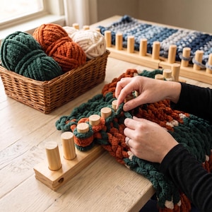 Può includere: Un telaio in legno con pioli verticali che sostiene filato spesso e voluminoso nei colori verde scuro, arancione bruciato e crema. Un cesto in vimini contiene gomitoli abbinati, mentre un secondo telaio mostra un progetto intrecciato blu.