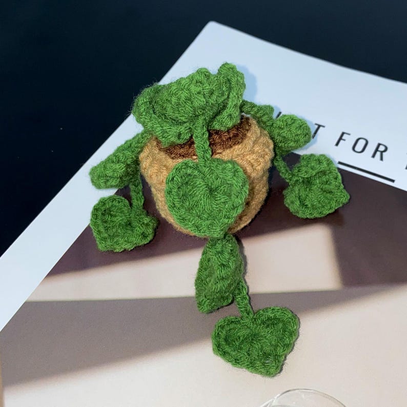 Puede incluir: Una planta de ganchillo hecha a mano con hojas verdes y una maceta marr&oacute;n. La planta tiene un dise&ntilde;o caprichoso, con hojas grandes en forma de coraz&oacute;n y hojas m&aacute;s peque&ntilde;as que se extienden desde la maceta. El trabajo de ganchillo es detallado y texturizado.