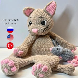 Puede incluir: Un gato de crochet de felpa hecho a mano en color beige con detalles en rosa en las orejas, la nariz y las patas. Un pequeño ratón gris de crochet está al lado del gato. El texto "pdf crochet pattern" es visible.