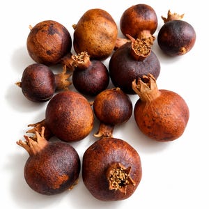 Op de afbeelding: Een verzameling gedroogde granaatappels met een textuurrijke, leerachtige schil in tinten van diepbruin, roest en donkerkastanjebruin. Elke vrucht heeft een opvallende, houtachtige kelk aan de bovenkant, wat zorgt voor een verwelkt, rustiek uiterlijk.