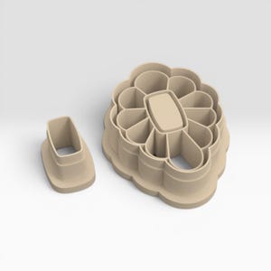 May include: Two beige cookie cutters. One is a rectangular shape, and the other is a flower shape with a rectangular center and petal-like cutouts. The cookie cutters are made of plastic and are designed for baking.