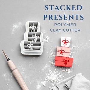 May include: White polymer clay cutter in the shape of stacked presents with bow details. A stack of three presents in red, pink, and white with red bows is also shown. The text reads "STACKED PRESENTS POLYMER CLAY CUTTER."