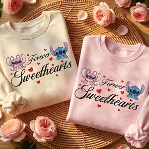 Może przedstawiać: Dwie bluzy z okrągłym dekoltem, jedna kremowa i jedna r&oacute;żowa, z napisem "Forever Sweethearts" i postaciami z kresk&oacute;wek. Projekt zawiera czerwone serca i postacie Stitcha i Anioła. Bluzy są prezentowane na tkanej macie z r&oacute;żowymi r&oacute;żami.