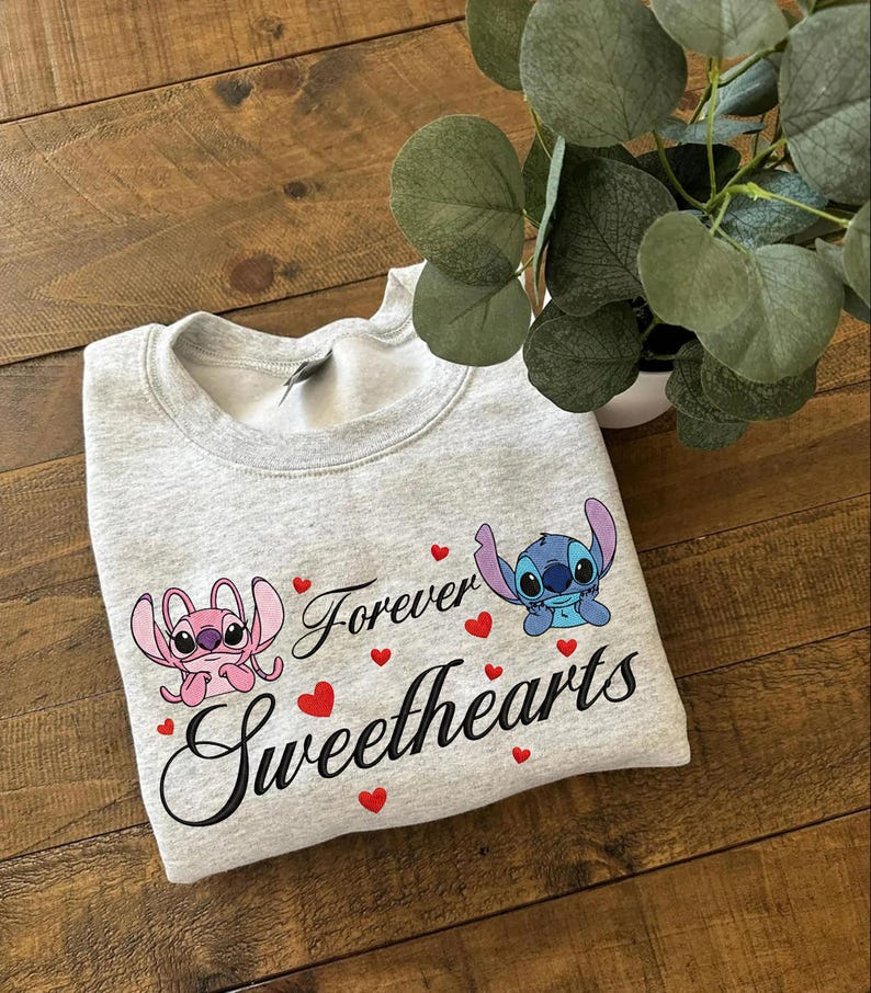 Może przedstawiać: Jasnoszara bluza z postaciami Angel i Stitch, napisami "Forever Sweethearts" i czerwonymi serduszkami. Bluza wykonana jest z miękkiego materiału.