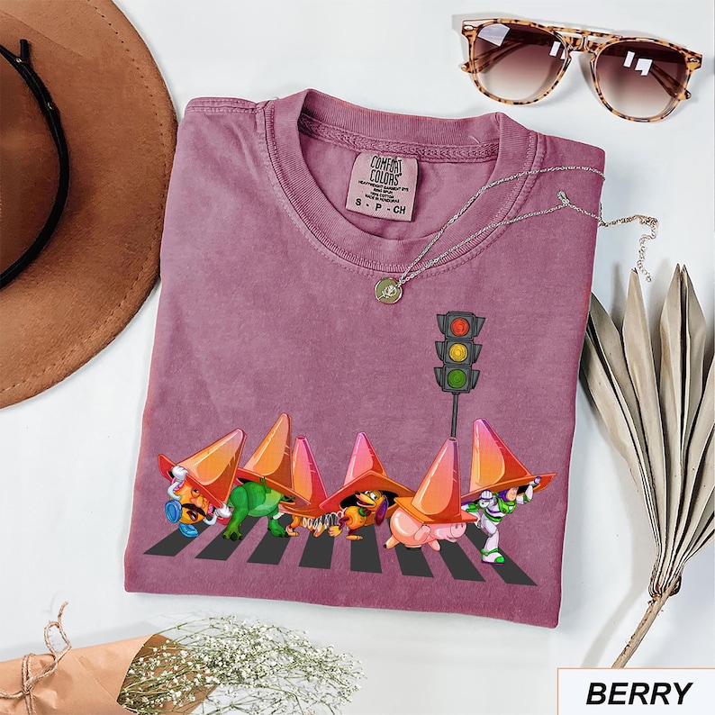 May include: Berry-colored t-shirt with a graphic of cartoon characters crossing a crosswalk under a traffic light. The shirt has a crew neck and short sleeves. The text "Comfort Colors" is on the tag.