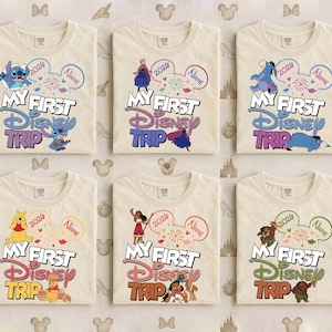 May include: Six cream-colored t-shirts with the text "MY FIRST DISNEY TRIP" in colorful lettering. Each shirt features a different Disney character and a customizable name bubble, with the year 2026.