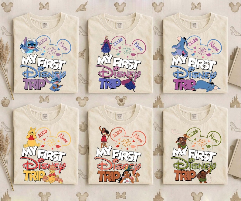 May include: Six cream-colored t-shirts with the text "MY FIRST DISNEY TRIP" in colorful lettering. Each shirt features a different Disney character and a customizable name bubble, with the year 2026.