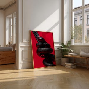 May include: A framed art print depicting a black snake wrapped around a katana blade, set against a red backdrop. The artwork is in a gold frame. The room has wooden flooring and a window, creating a bright, airy atmosphere.