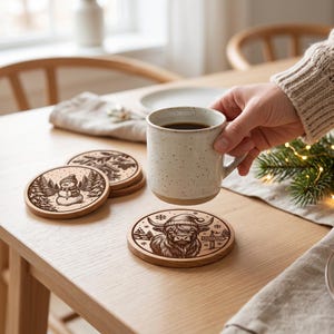 May include: A set of round wooden coasters featuring laser-engraved holiday designs, including a snowman in a forest, a birdhouse, and a Highland cow wearing a Santa hat with a North Pole sign, accompanied by a speckled ceramic mug.