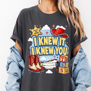 May include: A charcoal gray t-shirt featuring a graphic print with a yellow sheriff star labeled "INFINITY AND BEYOND," a red cowboy hat, red and white cowboy boots, alphabet blocks spelling "TS5U," and the text "I KNEW IT I KNEW YOU" and "you've got a friend in me."