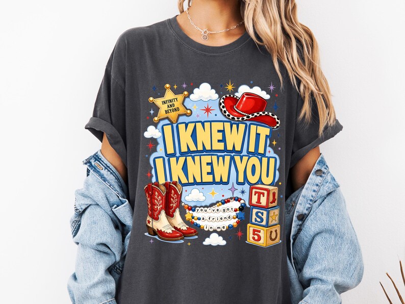 May include: A charcoal gray t-shirt featuring a graphic print with a yellow sheriff star labeled "INFINITY AND BEYOND," a red cowboy hat, red and white cowboy boots, alphabet blocks spelling "TS5U," and the text "I KNEW IT I KNEW YOU" and "you've got a friend in me."