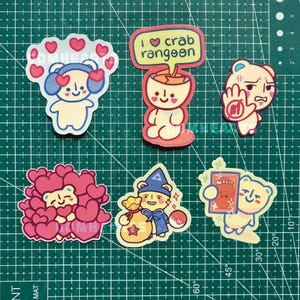 May include: Six die-cut stickers featuring a cartoon bear character in various poses. One bear wears headphones surrounded by hearts, another has a speech bubble saying I love crab rangoon, one holds a hand up, one is covered in hearts, one wears a wizard hat holding a bag, and one holds a magic card.