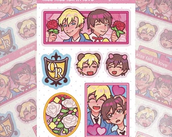 May include: A sticker sheet featuring anime-style illustrations with the text kiss kiss fall in love and gomhearts. Designs include two characters holding red roses, a shield with the letters OR, two character heads, and white roses in an oval.
